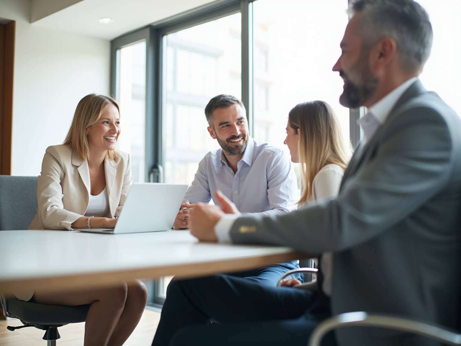 Four professionals talking around a conference table in a bright office with tall windows